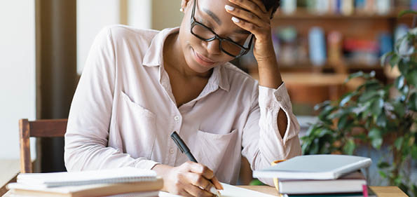 Beautiful black woman with pile of books taking notes during her studies at coffee shop  Industrious female student making home assignment, preparing for exam, writing coursework
