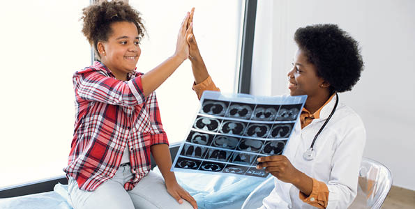 Healthcare and children  Radiology, MRI, computed tomography, x-ray concept  Friendly female African doctor showing an x-ray CT image to a young patient, 12-aged mixed race girl, giving high five